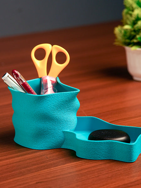 Turquoise desk organizer with scissors, pen, and black object on a wooden surface.
