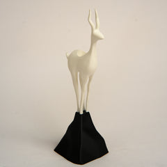 White deer figurine on a black stand against a beige background