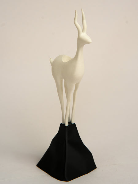 White deer figurine on a black stand against a beige background